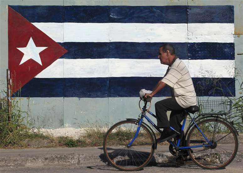 Ciclista passa em frente à bandeira cubana em Havana em imagem de dezembro de 2012