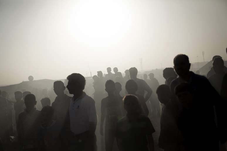 Em meio &agrave; fuma&ccedil;a. refugiados observam o fogo consumir uma barraca