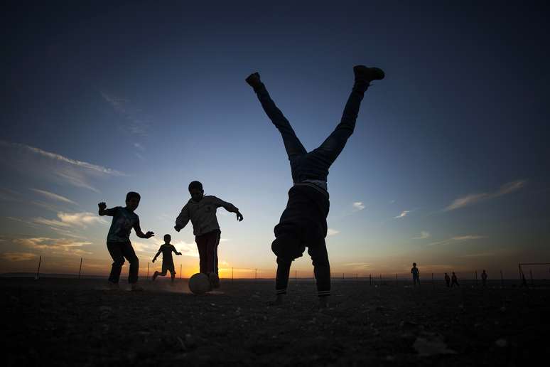 Crian&ccedil;as brincam e jogam futebol durante enquanto o sol se p&otilde;e no deserto da Jord&acirc;nia