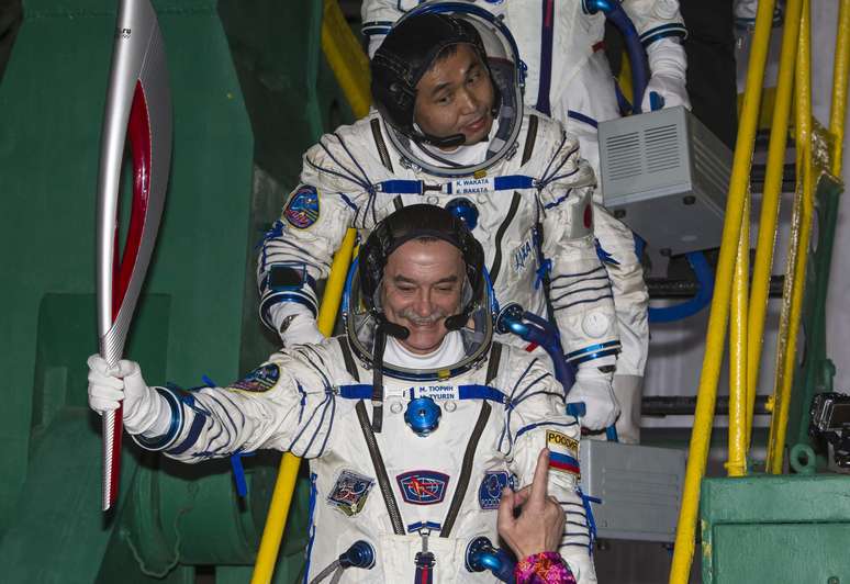 Com a tocha olímpica, russo Mikhail Tyurin sorri antes de entrar na nave espacial