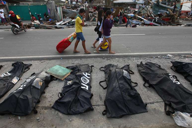 <p><strong>13 de novembro -</strong> Pessoas cobrem os narizes ao passarem por corpos enfileirados em Tacloban</p>