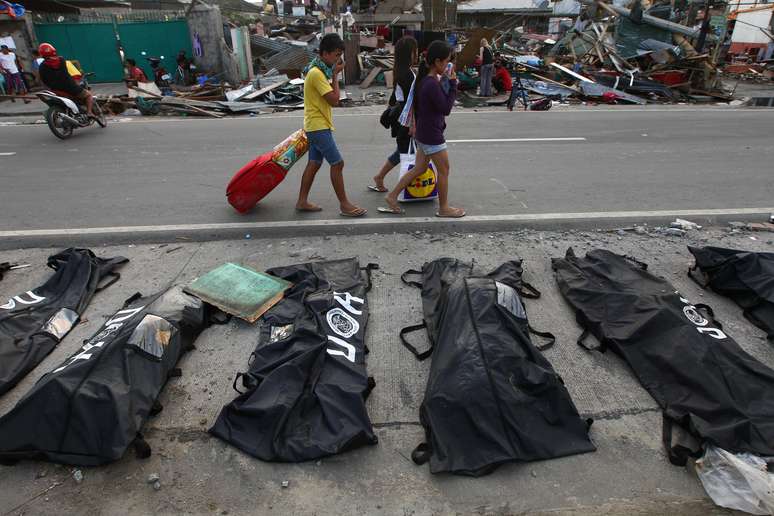 <p>Pessoas cobrem os narizes ao passarem por corpos enfileirados em Tacloban</p>