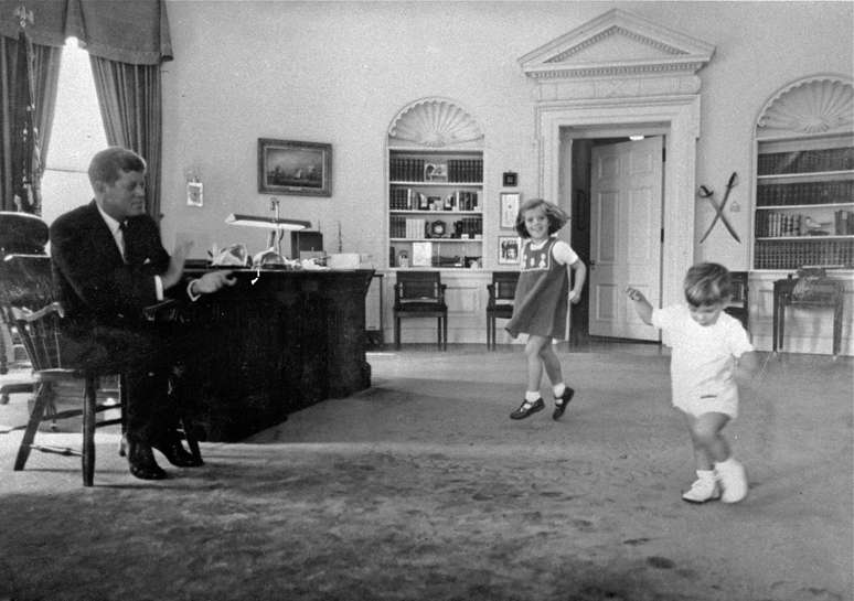 Em foto de outubro de 1962, Kennedy aplaude enquanto seus filhos Caroline e John dançam no Salão Oval da Casa Branca