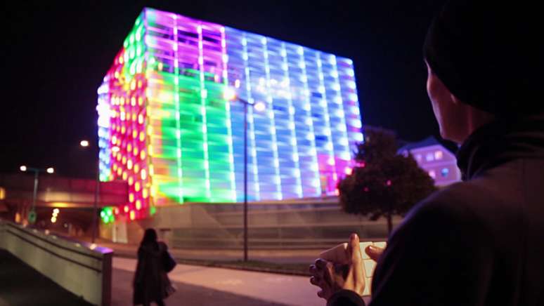 Jogador mexe em um cubo mágico todo branco e movimenta as cores projetadas no prédio