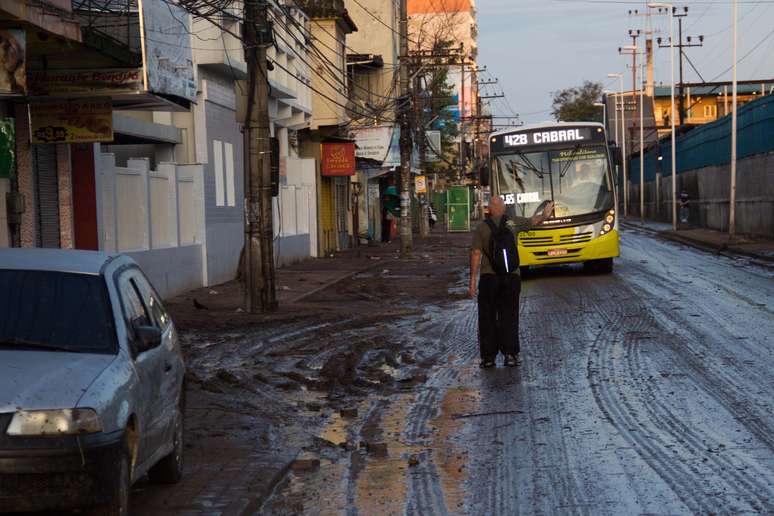 Morador de Nova Iguaçu espera o ônibus em rua coberta por lama, na Baixada Fluminense