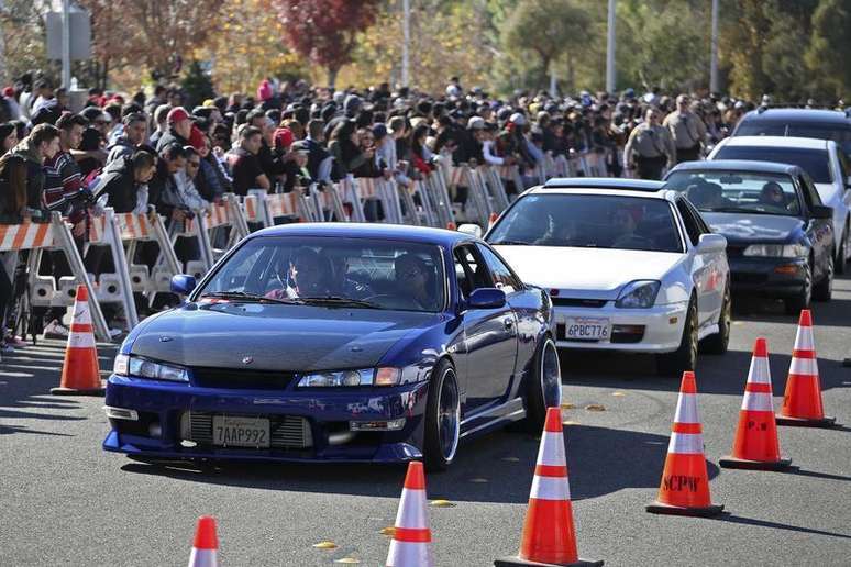 Veículos são conduzidos em meio a uma multidão em evento não oficial em memória do astro Paul Walker do filme "Velozes e Furiosos", Califórnia, 8 de dezembro de 2013. Milhares de fãs, alguns guiando carros envenenados, reuniram-se no domingo no local do sul da Califórnia onde o ator Paul Walker morreu em um acidente automobilístico na semana passada. 08/12/2013