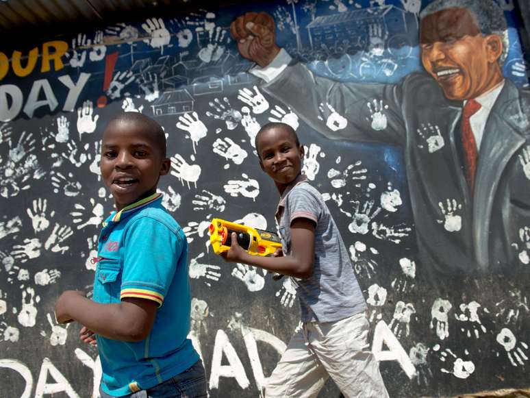 Crian&ccedil;as brincam e sorriem em frente a mural a 'Madiba'