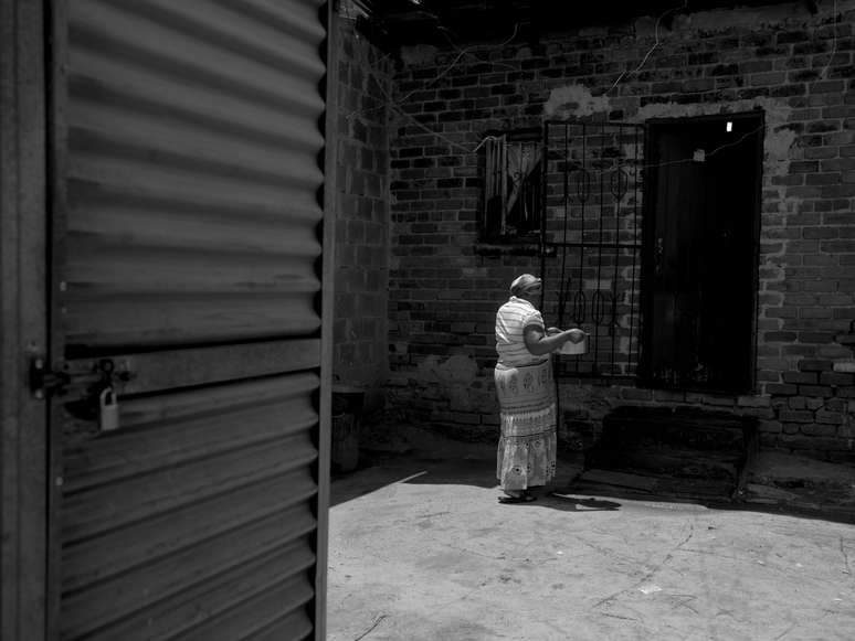 <p>Mulher carrega panela com água para sua cada na favela de Alexandra, em Johannesburgo, na África do Sul. Água e o banheiro - porta do lado esquerdo - é dividido por cerca de 250 moradias.</p>