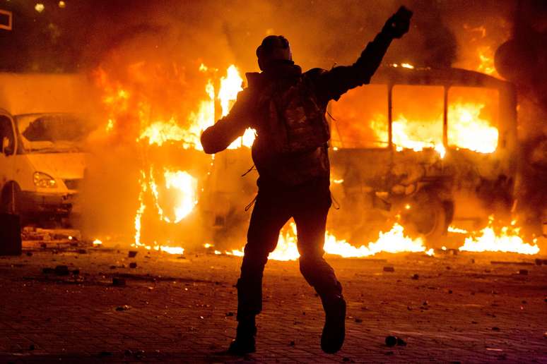 <p><strong>19 de janeiro - </strong>Manifestante atira pedra em ônibus da polícia em chamas</p>