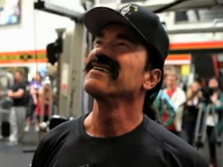 Arnold Schwarzenegger disfarçado como Howard observa um retrato seu na academia Gold's Gym em Venice Beach