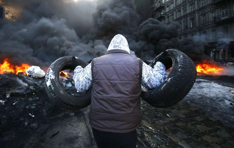 Manifestante leva mais pneus para a fogueira acesa no centro de Kiev