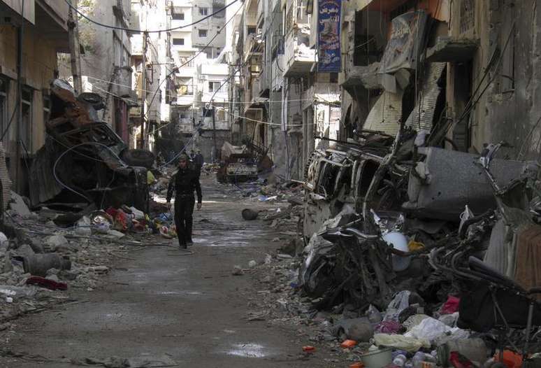 <p>Homem caminha por entre pr&eacute;dios destru&iacute;dos em uma &aacute;rea sisitada de Homs</p>