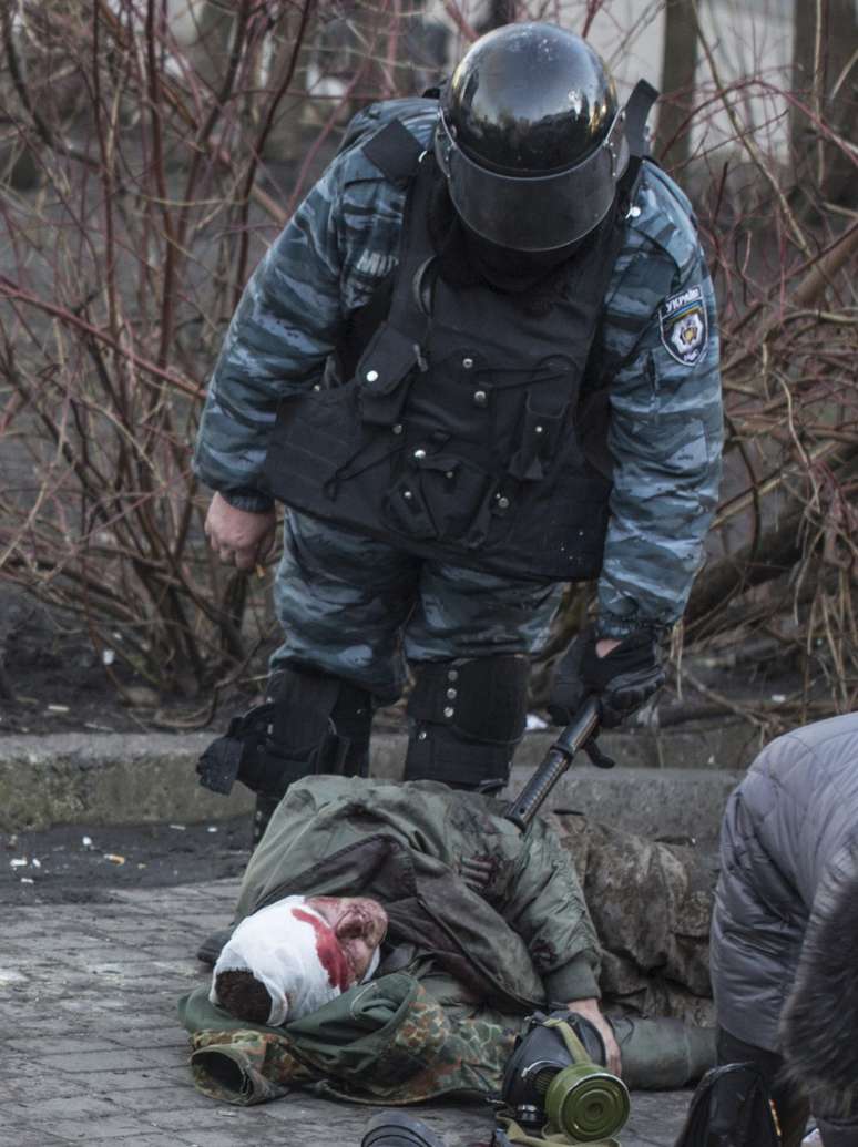 Policial observa manifestante ferido durante confrontos no centro de Kiev