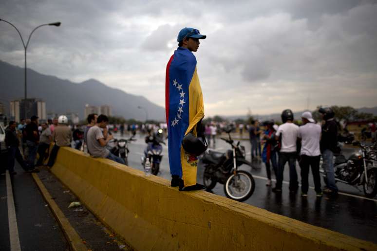 Manifestante vestindo bandeira venezuelana durante protesto da oposição que bloqueou ruas próximas ao aeroporto La Cartola, em Caracas, em 18 de fevereiro