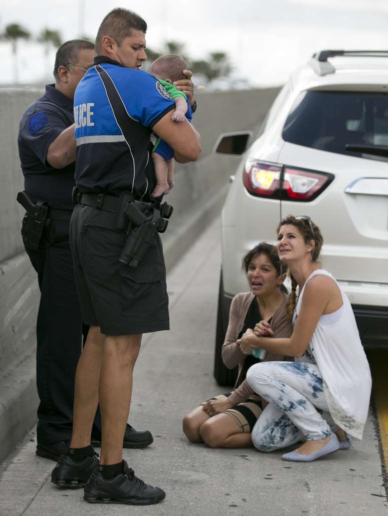 O policial Amauris Bastidas segura Sebastian, enquanto uma motorista (à esquerda) conforta a tia do menino