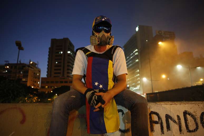 Manifestante antigoverno senta sobre muro enquanto protestos bloqueiam rua em Caracas