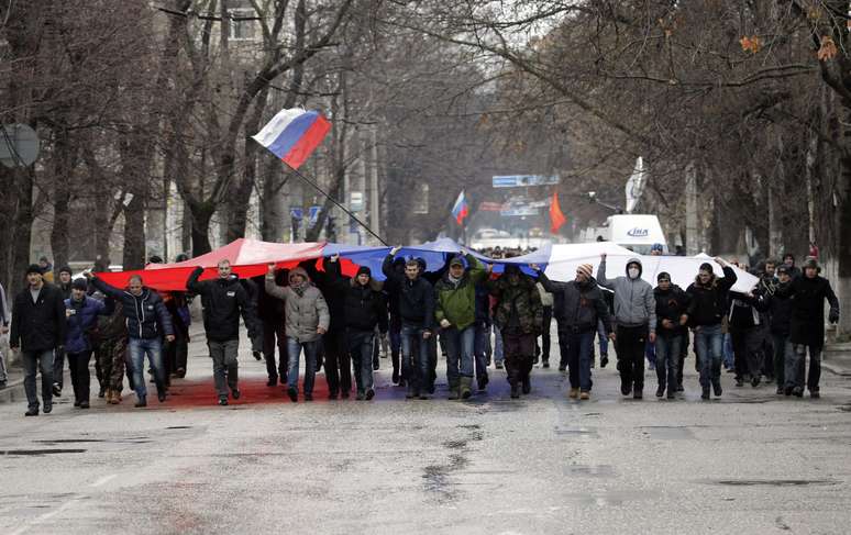 <p>Segurando uma bandeira russa, manifestantes marcham em frente ao prédio do governo, na Crimeia. De acordo com o Ministro do Interior ucraniano, a polícia está em alerta máximo depois que dezenas de manifestantes invadiram o edifício do Parlamento de Simferopol</p>