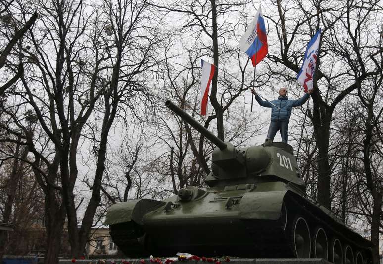 <p>Manifestante exibe bandeiras da Rússia e da Crimeia em um antigo tanque das Forças Armadas da União Soviética, durante protesto em frente ao prédio do governo de Simferopol, na Crimeia</p>