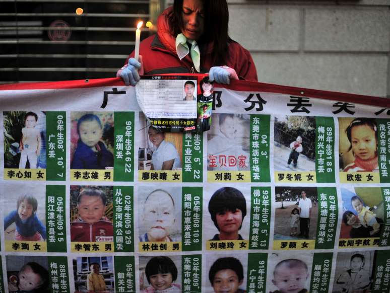 <p>Mulher segura vela e&nbsp;um cartaz que mostra fotos de crian&ccedil;as desaparecidas, na prov&iacute;ncia central chinesa de Hubei, em 24 de janeiro 2010</p>