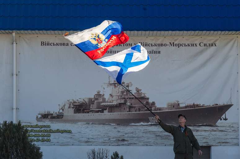 <p>Ativista russo agita bandeiras da Rússia e da Marinha russa em frente à entrada do Comando Geral da Marinha ucraniana em Sebastopol, na Ucrânia</p>