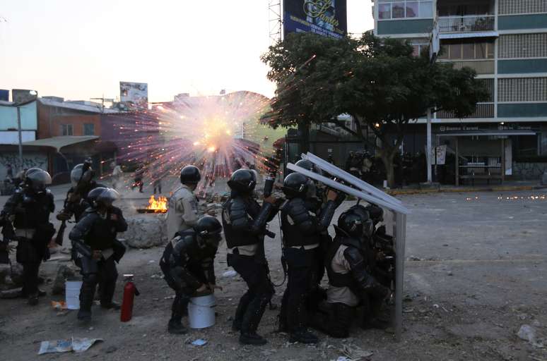 Oficiais da Polícia Nacional Bolivariana se protegem da explosão de um artifício lançado por manifestantes anti-governo durante confrontos em Caracas, em 5 de março