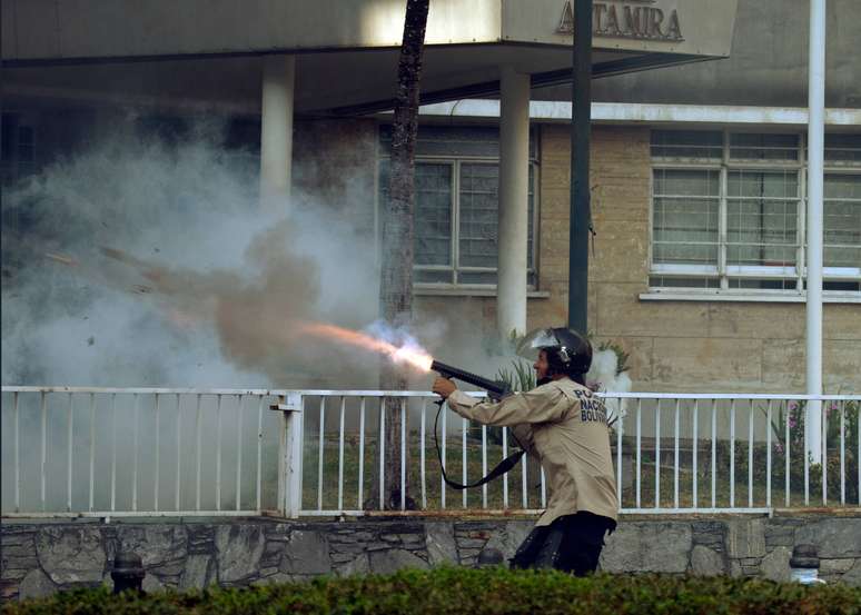 Oficial da Guarda Nacional Bolivariana atira gás em manifestantes durante protesto em Caracas, neste sábado, 8 de março