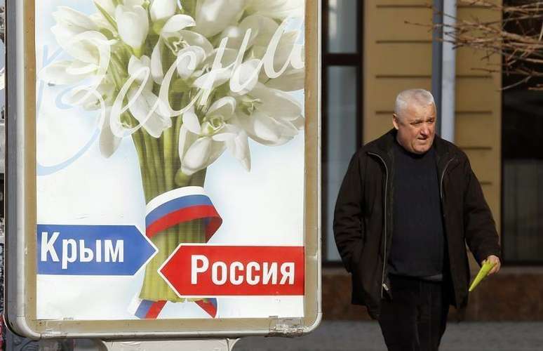 <p>Um homem passa na frente de um pôster com os dizeres "Crimeia - Rússia", em Simferopol</p>