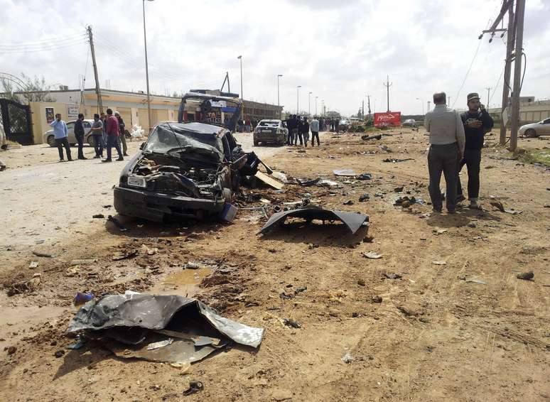 Homens observam carro destruído por explosão de bombas que mataram pelo menos 5 e feriram outros 10 na cidade de Benghazi, ao leste da Líbia