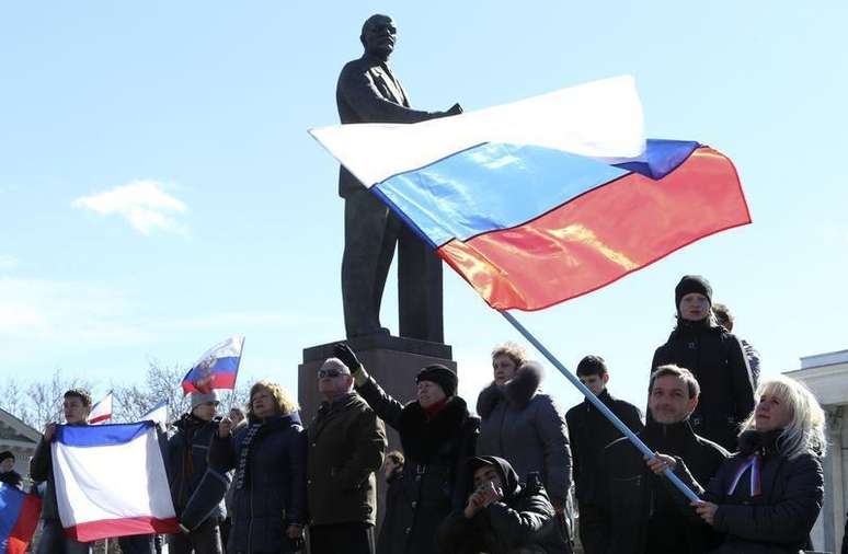 Participantes de uma manifestação pró-Rússia agitam bandeiras russas na frente da estátua de Lenin, em Simferopol. Os ministros das Relações Exteriores da União Europeia concordaram em impor sanções contra 21 pessoas da Rússia e da Ucrânia nesta segunda-feira, incluindo proibições de viagens e congelamento de bens, disse o chanceler da Lituânia nesta segunda-feira. 17/03/2014