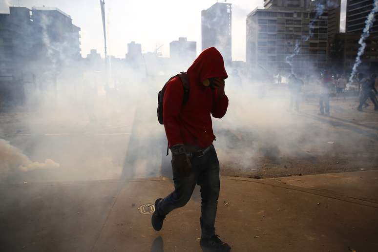 <p>Manifestante anti-governo foge&nbsp;de g&aacute;s lacrimog&ecirc;neo usado pela guarda nacional contra protestos na pra&ccedil;a de Caracas, neste domingo</p>