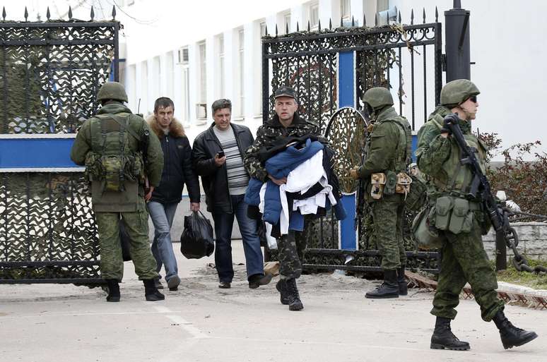 <p>Ucranianos carregam seus pertences passando ao lado de soldados russos na base naval de Sebastopol</p>