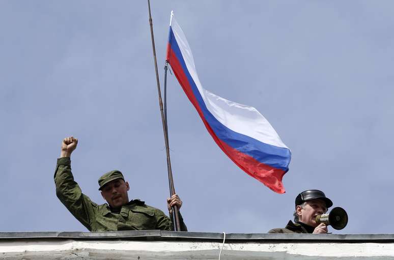 Homem segura uma bandeira russa no telhado da base naval de Sebastopol nesta quarta-feira
