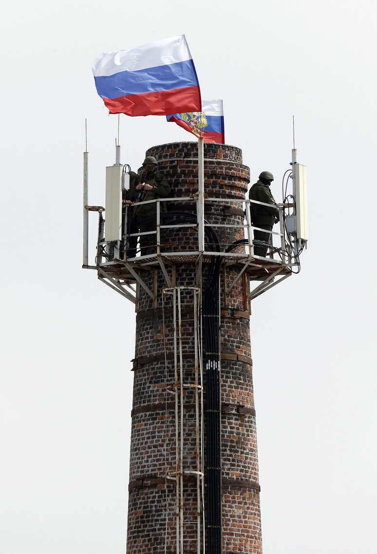 <p>Homens armados hasteiam a bandeira russa no topo de uma chaminé da base nava de Sebastopol - tomada pelos russos sem disparos na manhã da última quarta-feira</p>