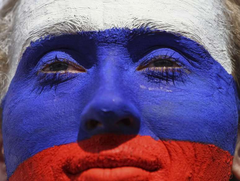 Manifestante pinta a cara com as cores da bandeira russa durante protestos neste sábado. Nos cartazes, pró-russos pedem volta do ex-presidente da Ucrânia refugiado na Rússia