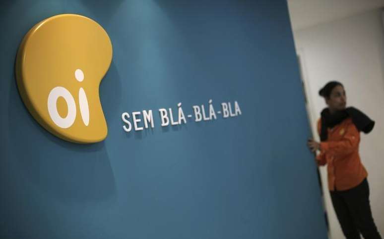 Uma mulher parada ao lado do logotipo da Oi, em uma loja em São Paulo. A Comissão de Valores Mobiliários (CVM) decidiu na terça-feira que os controladores da operadora Oi poderão votar em assembleia sobre a fusão com a Portugal Telecom, contrariando o pedido dos acionistas minoritários da companhia, mostrou a ata de reunião do colegiado do órgão regulador divulgada na noite da véspera. 02/10/2013