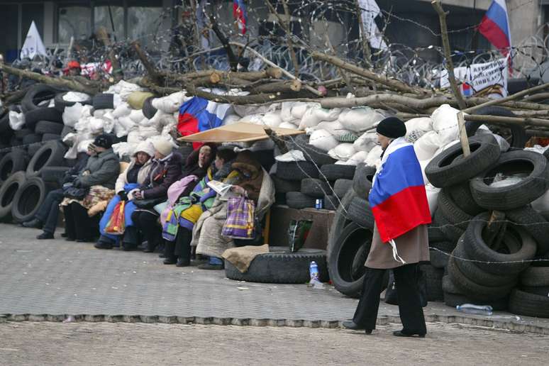 <p><strong>9 de abril -</strong> mulher envolvida por uma bandeira russa caminha em frente à barricada montada em Donetsk</p>