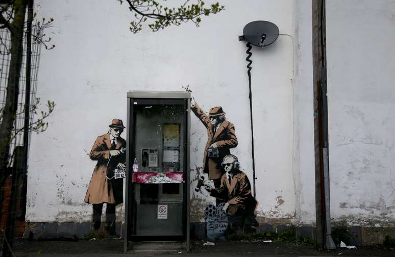 Um estêncil que seria do artista Banksy se tornou atração turística em Cheltenham, na Inglaterra. Na obra, homens que aparentam serem detetives "investigam" a cabine telefônica.