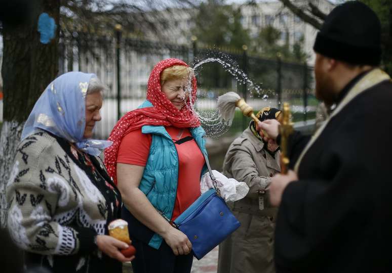 <p>Um sacerdote ortodoxo ucraniano borrifa água benta sobre os fiéis antes de um culto de Páscoa na cidade ucraniana oriental de Slaviansk </p>