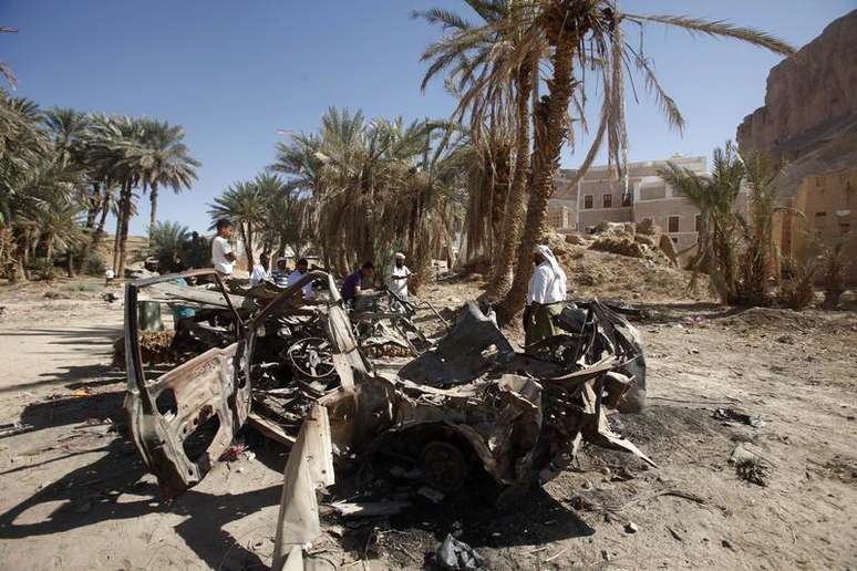 Pessoas se reúnem perto de um carro destruído por um ataque aéreo de um drone dos EUA; alvos foram militantes da Al-Qaeda em agosto de 2012