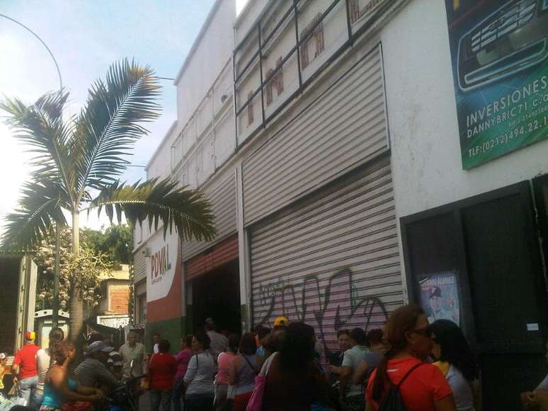 <p>Uma fila de compradores espera do lado de foram de uma loja pública à espera da entrega de mercadorias que poderia acontecer na terça-feira à noite</p>