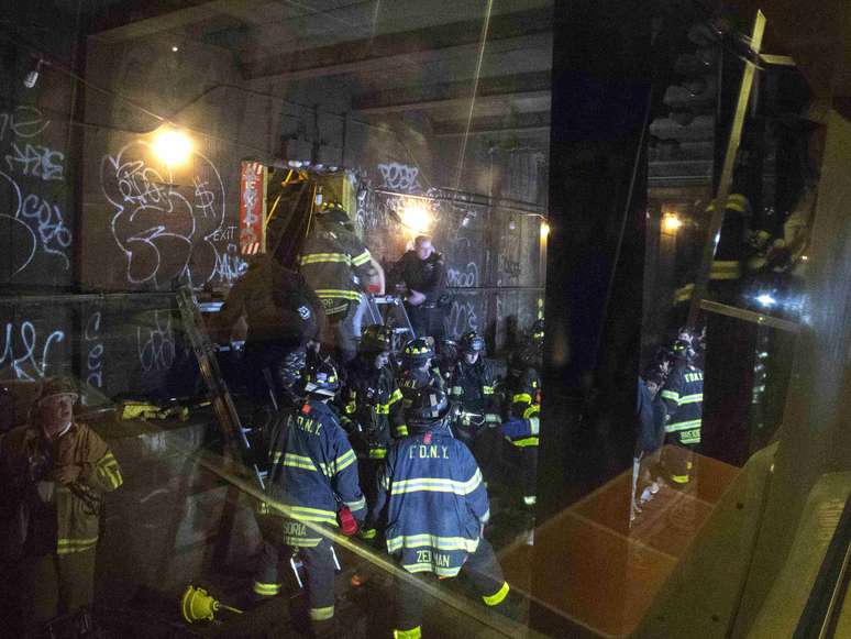 <p>Equipes de resgate são vistas através da janela de um dos vagões descarrilados. Os passageiros deixaram o local por uma saída de emergência do túnel do metrô</p>