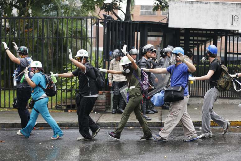 <p>Manifestantes anti-governamentais, que trabalham como paramédicos, andam com as mãos para cima ao passar por policiais da Guarda Nacional, durante os confrontos em Los Palos Grandes Caracas, em 8 de maio</p>