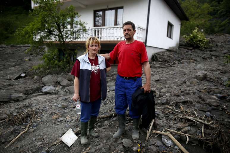 Casal fica em frente a sua casa na cidade de Topcic Polje, Bósnia; país calcula prejuízos de milhões de reais