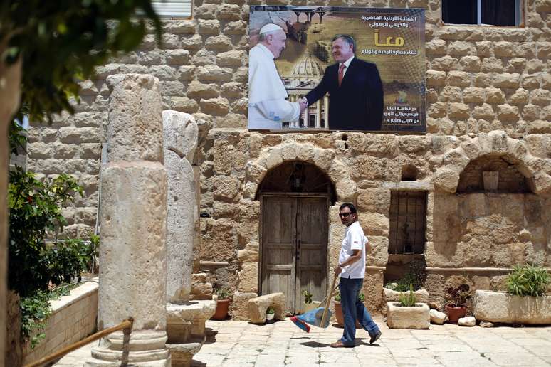 <p>Trabalhador passa em frente a um cartaz com retratos do Papa Francisco e o rei Abdullah da Jordânia, no pátio da Igreja católica São João Batista, onde, segundo a Bíblia, João Batista foi detido. Foto tirada em 23 de maio, na cidade de Madaba, a sudoeste da capital da Jordânia, Amã</p>