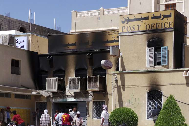 <p>Pessoas se reúnem do lado de fora de um posto do correio danificado depois de ter sido invadido por homens armados na cidade de Seyoun, na província sudeste iemenita de Hadramout, neste sábado, 24 de maio</p>