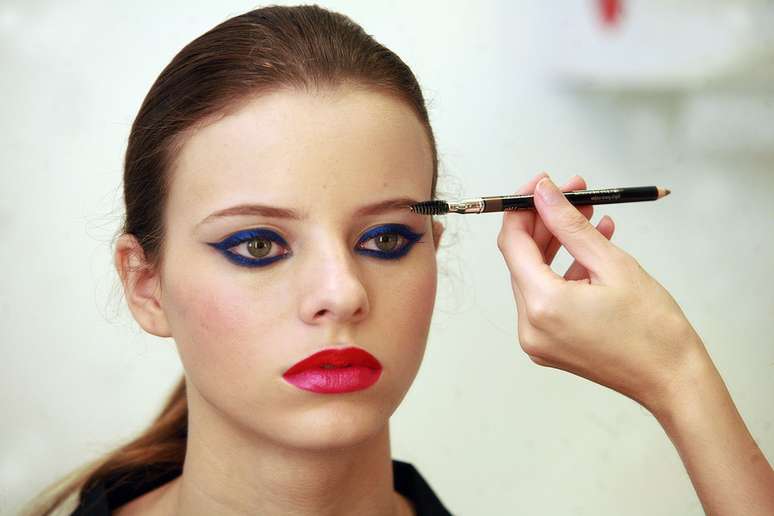 A maquiagem fica vibrante por conta da combinação dos tons vermelho e pink, do batom, e do azul nos olhos