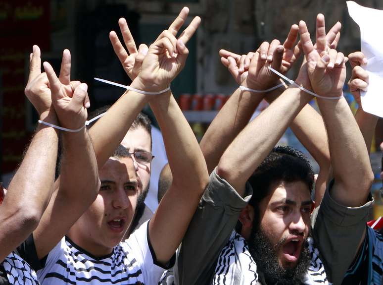 <p>Palestinos amarram as m&atilde;os e&nbsp;gritam slogans durante uma manifesta&ccedil;&atilde;o de solidariedade aos prisioneiros palestinos detidos sem julgamento&nbsp;em pris&otilde;es israelenses, na cidade de Nablus, na Cisjord&acirc;nia, em 26 de maio</p>