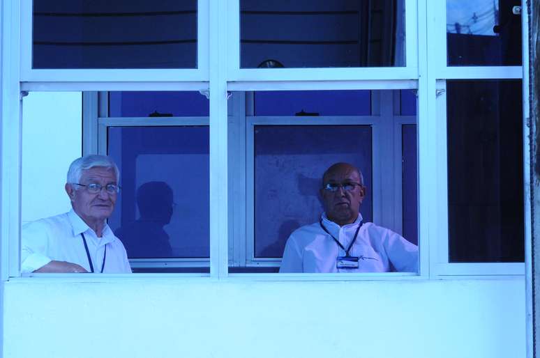 Angelo Martinelli (E), porteiro da instituição há oito anos, passa as oito horas de expediente de olho nas obras da avenida e do estádio