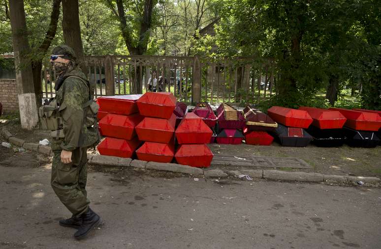 <p>Separatista caminha pr&oacute;ximo aos caix&otilde;es com os corpos dos colegas mortos em confronto com for&ccedil;as de seguran&ccedil;a ucranianas perto do aeroporto de Donetsk, em 29 de maio</p>