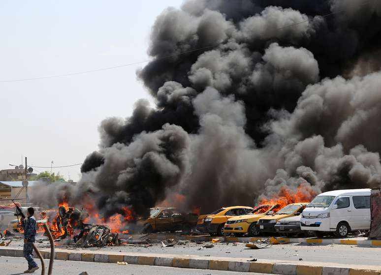 <p>Policial iraquiano &eacute;&nbsp;fotografado ao lado de ve&iacute;culos em chamas&nbsp;momentos ap&oacute;s uma&nbsp;s&eacute;rie de bombas atingirem&nbsp;o reduto xiita de Sadr City, em Bagd&aacute;, no Iraque, em 13 de maio</p>